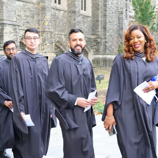 four students in black graduation robes walking outside