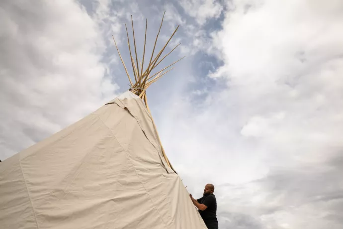 Tipi against cloudy sky with bearded man closing adjusting the canvas