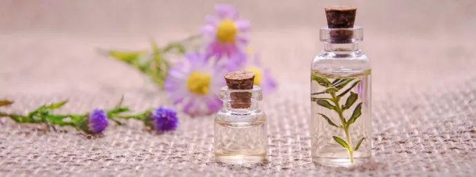 Two bottles of perfume, with purple and yellow flowers in the background. Image from Pixabay.