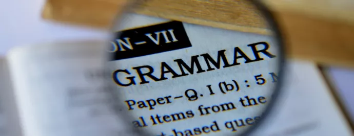 A magnifying glass pointed an open book over the word "grammar".