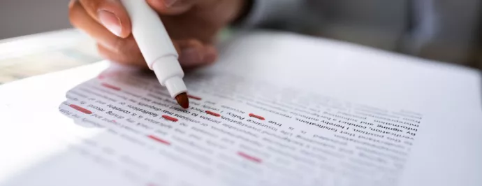 A closeup image of a student highlighting text in red.