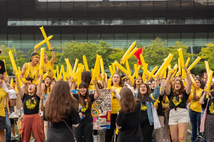 Group of students standing outside cheering and waving yellow inflatable batons