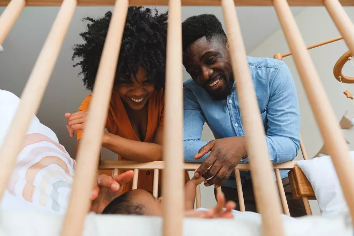 mother and father play with infant in a crib