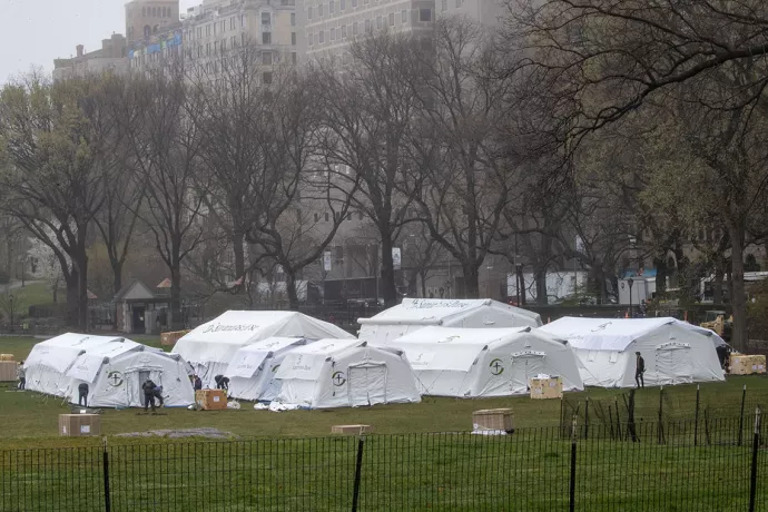 Large white tents in field with people working around them, apartment buildings in background