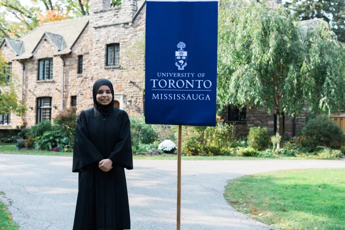Mahera Islam in black gown standing next to flag that reads University of Toronto Mississauga
