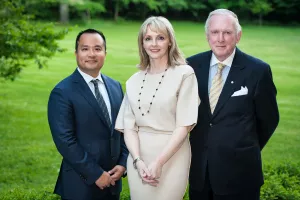 Two men and a woman in business attire pose in a green garden