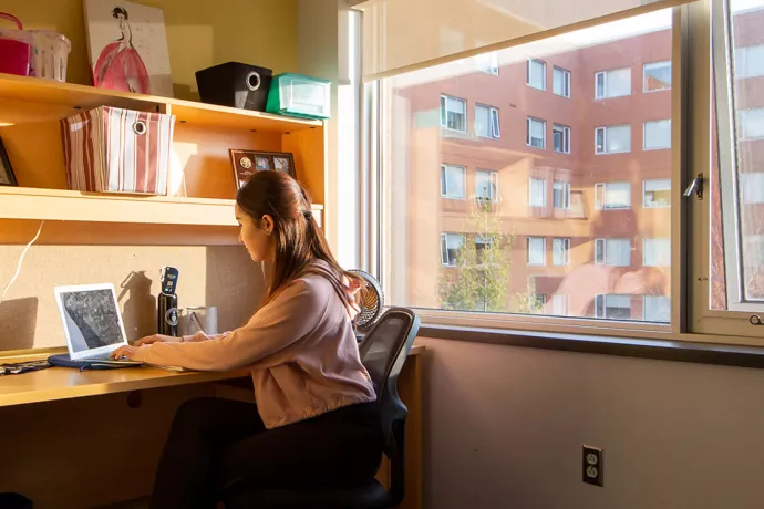Student sitting at desk in residence room near window