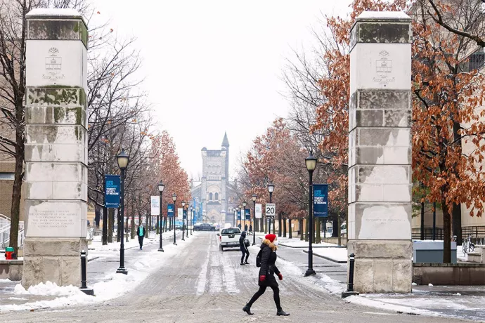 Person in red hat, wearing mask, walking past entrance to St. George campus on a snowy day