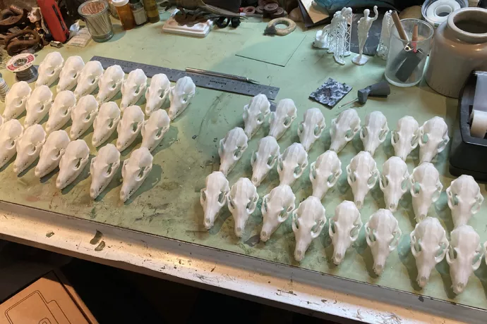 About 45 3d printd skills, lined up in three rows, on a work desk with a ruler, tape dispenser and unknown partial 3D model