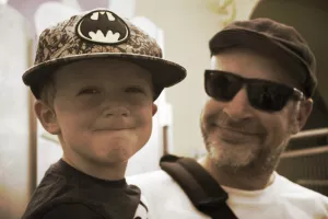 Man with hat and sunglasses holding a smiling child wearing a baseball hat