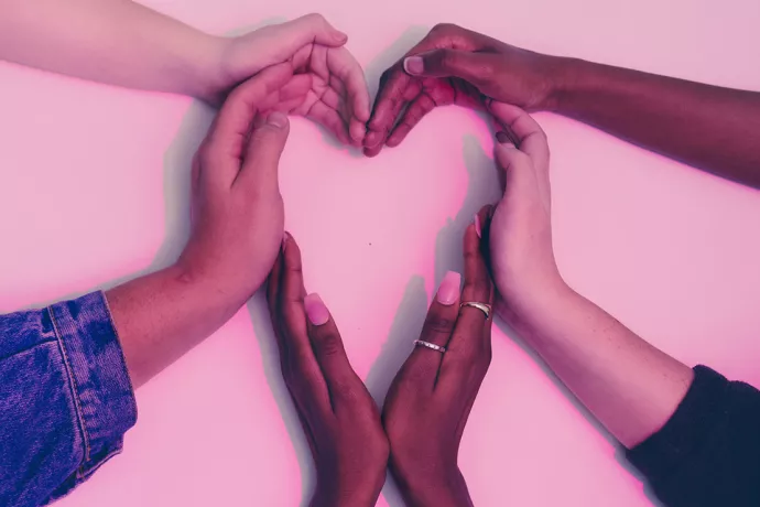 Three pairs of hands coming into the middle of the frame to create a heart against a white backdrop