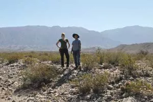 Jeremy Rimando and Lindsay Schoenbohm stand on a rocky plain with mountains in the background