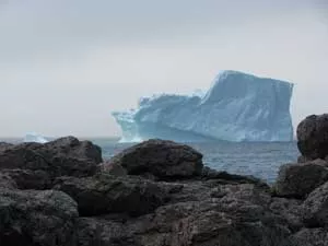 Image of domed rocks along a coast. There is a large iceberg in the background.