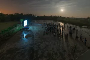 Aerial photograph of a crowd of people watching a film on a screen in a parking lot.