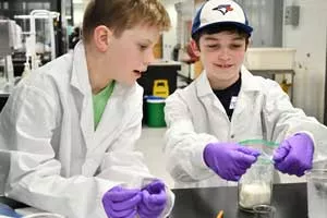 Two boys wear lab coats as they make ice cream in a UTM chemistry lab.