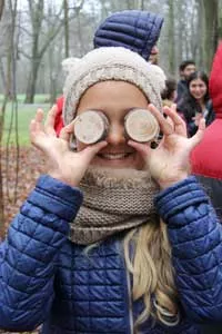 A smiling girl holds two wood discs over her eyes as if they were glasses.