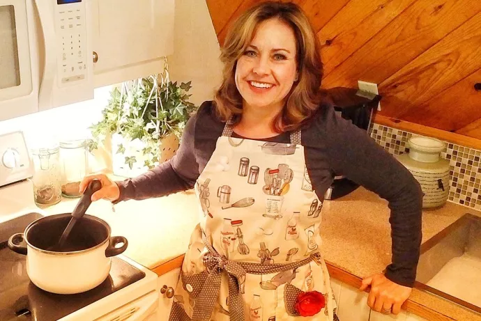 Kimberly Green standing by her stove, stirring a pot, smiling at camera