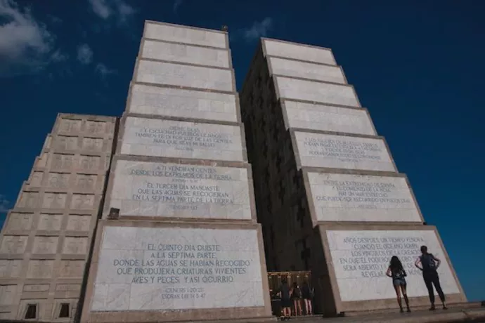 Two square, stepped concrete columns rising into the sky with illegible inscriptions. Two students standing below, looking up at towering edifice.