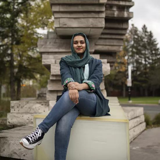 Amna Adnan sitting on the end of the stone entrance to UTM, smiling at the camera.