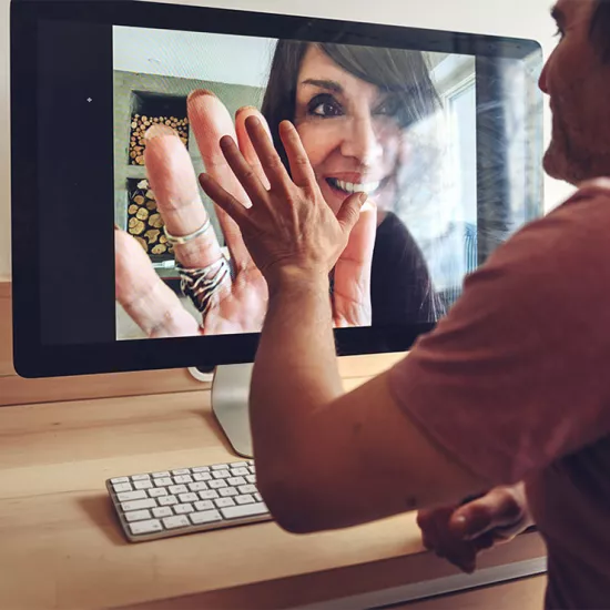 Man waving at woman on computer screen, who is waving back