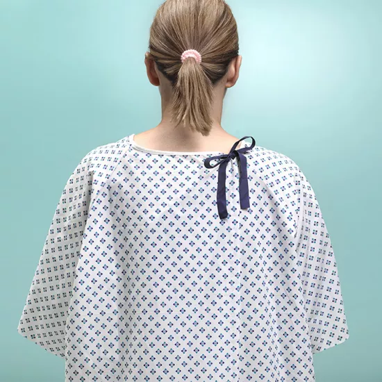 Woman in hospital gown standing with back to camera, hair in ponytail