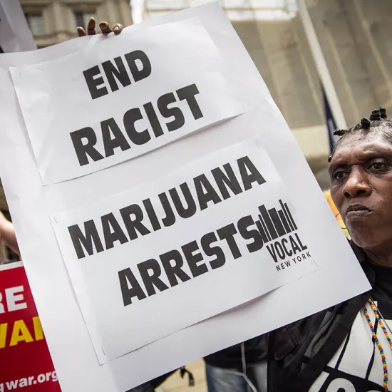 protestor holds sign that says end racist marijuana arrests. Sign in background held by another protestor reads No more biased policing.
