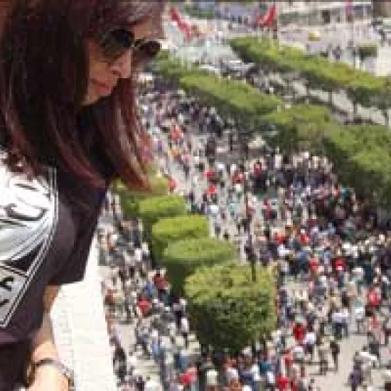 Woman looks down over a crowd protesting in the street. She is wearing a shirt that reads "Disobey" in English and Farsi