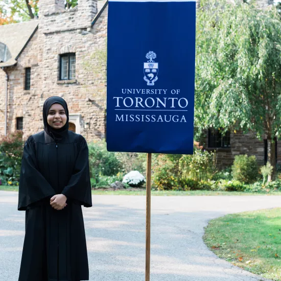 Mahera Islam in black gown standing next to flag that reads University of Toronto Mississauga