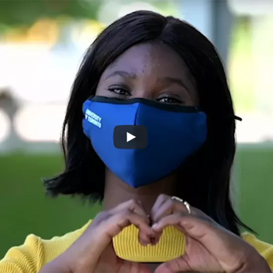 Girl wearing U of T face mask looking into camera, her hands making a heart symbol