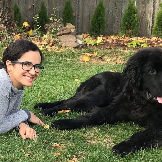 Sofia laying on grass beside a large, black Newfoundland dog