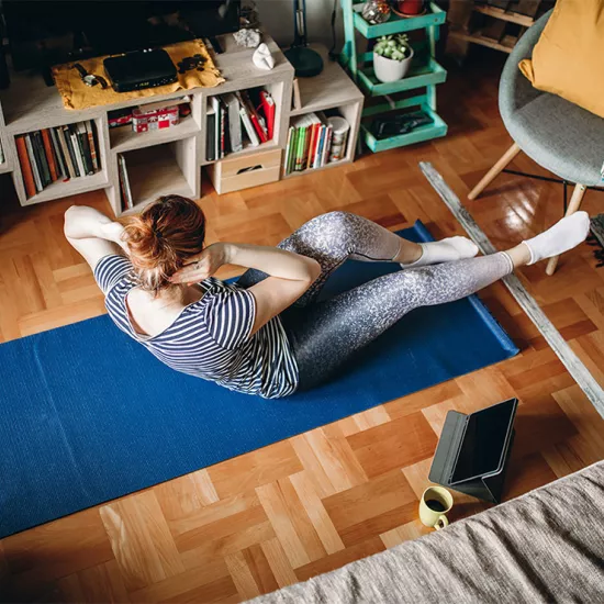 Overhead shot of woman on yoga mat next to a bookcase and couch, coffee and tablet on floor next to her