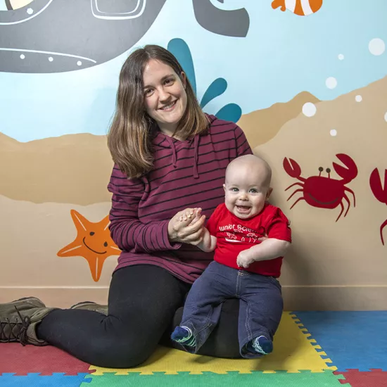 Laura Cirelli sitting in front of a colourful wall mural with starfish and crabs holding her son Ian