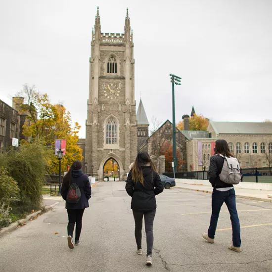 Three students walking away from camera toward old building