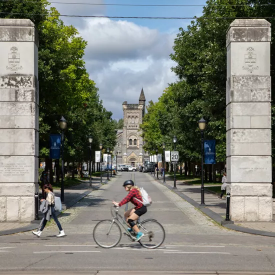 Person in red cycling in front of two concrete pillars leading into U of T campus