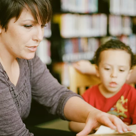 Woman helping a young boy read a book