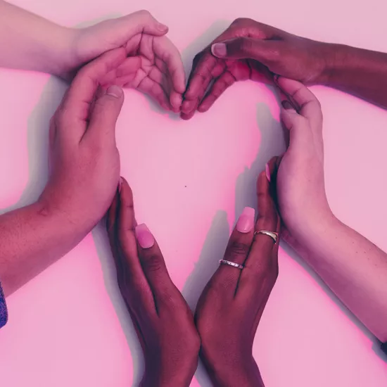Three pairs of hands coming into the middle of the frame to create a heart against a white backdrop