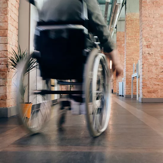 Individual in wheelchair moving away from camera in hallway with brick pillars on either side