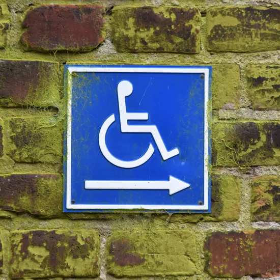 Brick wall with blue sign with white line drawing of wheelchair and an arrow pointing right