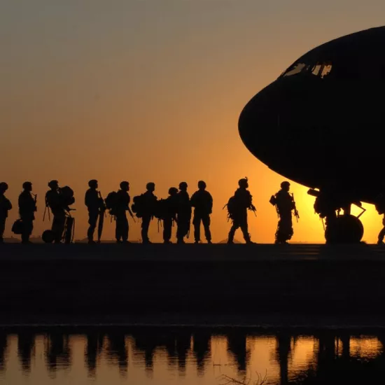 silhouette of soldiers boarding a military plane against a setting sun