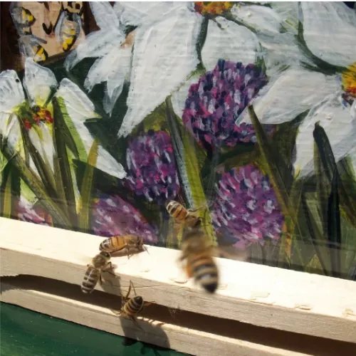 bees outside their hive by a wall with a flower mural