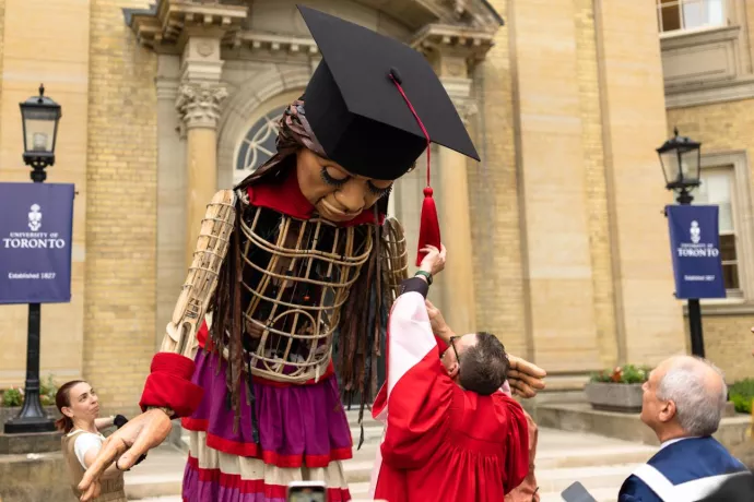 Little Amal has her mortarboard tassel adjusted outside Convocation Hall (Photo by Nick Iwanyshyn)