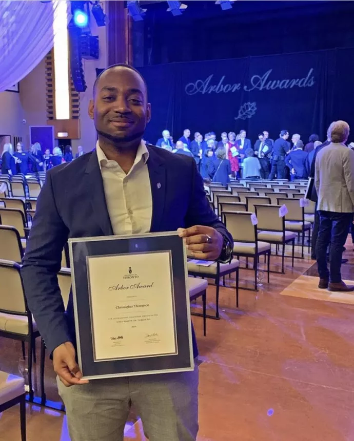 Chris stands smiling at the Arbor Awards celebration, holding his award. 