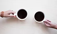 Two hands holding coffees on a table