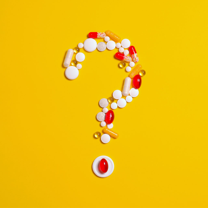various pills shaped into a question mark against a yellow background