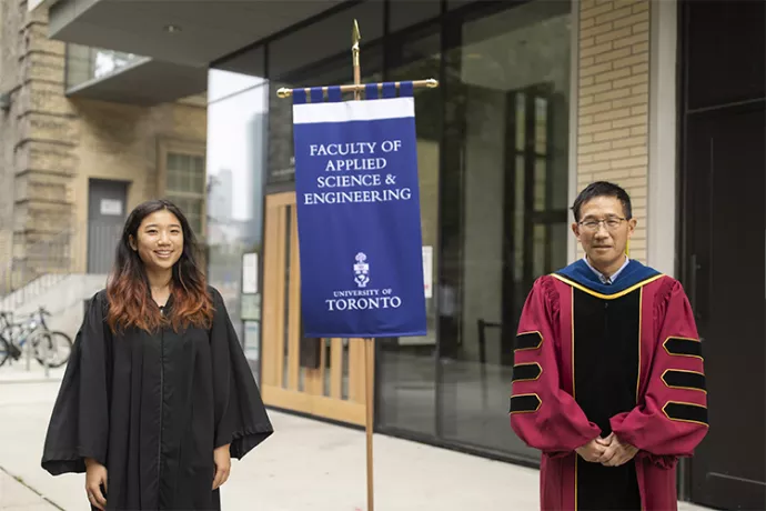 Student in black grad gown standing on the left, professor in red gown on the right, between them is a flag that reads faculty of applied science and engineering university of toronto