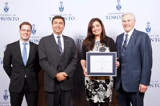 Photo of Samra Zafar holding a framed award certificate; 3 men standing next to her