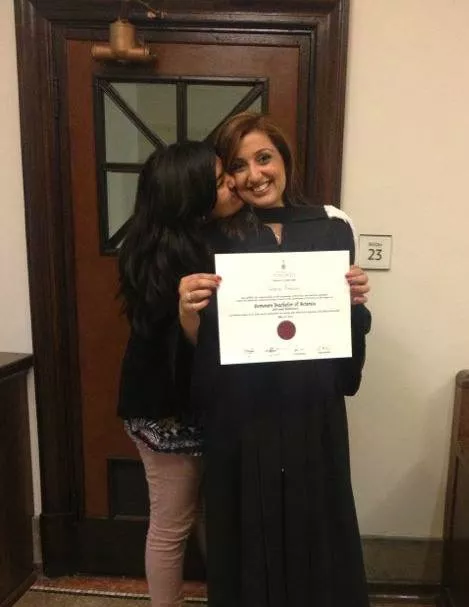 Samra Zafar with one of her daughters. Samra is wearing a cap and gown and is holding her graduation certificate