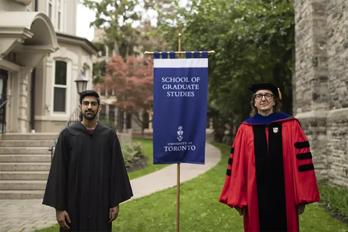Student in black grad gown standing on the left, professor in red gown on the right, between them is a flag that reads School of Graduate Studies university of toronto