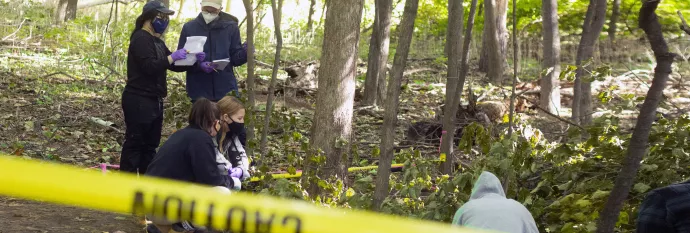 students in the woods with yellow caution tape in the foreground