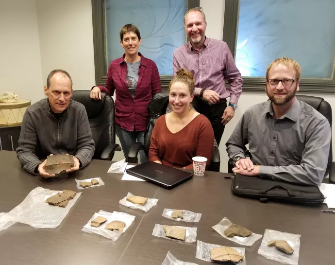 five people around a table containing pottery artifacts